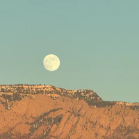 a full moon rises over a mountain range